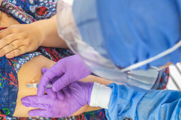 Top view of the hands of a doctor or nurse with surgical gloves, mask and face protection vaccinating a person in his arm with a syringe. Vaccination and coronavirus concept