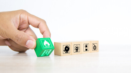 Close-up hand choose fire prevent symbol on wooden toy block stacked with door exit sing or fire escape icon with fire extinguisher and emergency protection for safety prevention and rescue.
