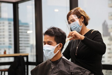 Barber and customer wearing facial mask in hair salon while having a haircut for avoiding contagion...