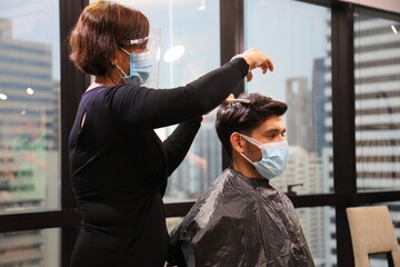 Barber and customer wearing facial mask in hair salon while having a haircut for avoiding contagion...