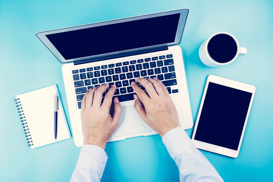 Hand of businessman working on laptop computer with tablet and notebook on desk in office, hand typing keyboard with book and pen, workplace with copy space, top view, flat lay, business concept.
