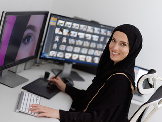 Muslim female graphic designer working on computer using graphic tablet and two monitors