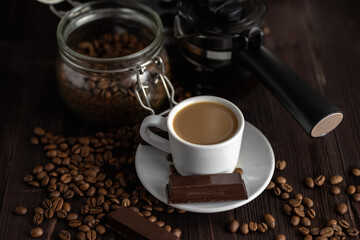 A cup of coffee with chocolates and coffee beans on a wooden table.