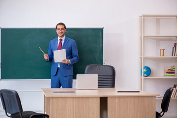 Young male teacher in suit in front of green board