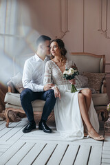 Young bride and groom in lace dress posing while sitting on the armchair.