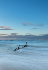 Rusting remains of ship wreck awash on the beach at sunset