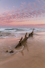 Rusting remains of ship wreck awash on the beach at sunset