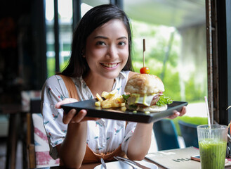 Asian women smiling and happy and enjoyed eating hamburgers at coffee and restaurant on relax time