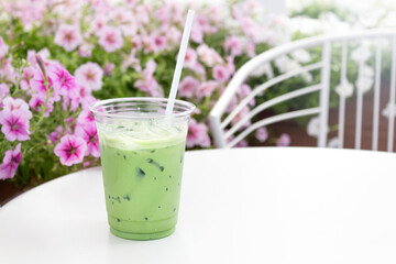 Matcha ice green tea latte in take away cup against blossom flowers.