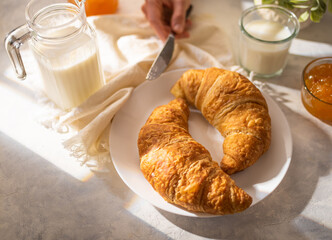 Breakfast in the morning. Morning light, two croissants, orange jam, milk. Hands of the girl at breakfast. Hospitality business. Breakfast in french style.