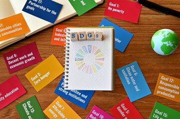 There is a table with a card with the SDG goals and a ball of earth, a small sketchbook with SDG symbols and a wooden cube stamped with the letters SDGs.