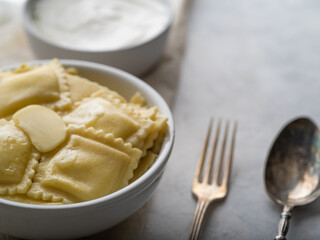 Italian ravioli or dumplings, Russian pelmeni. With sour cream on a light background with space