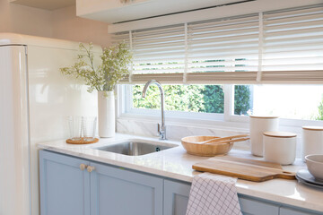 Clean new sink in stylish kitchen interior by the window. Wooden utensils and ceramic vase with...