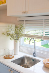 Clean new sink in stylish kitchen interior by the window. Wooden utensils and ceramic vase with flower on kitchen counter.