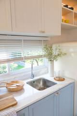 Clean new sink in stylish kitchen interior by the window. Wooden utensils and ceramic vase with flower on kitchen counter.