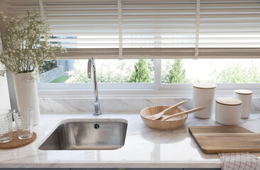 Clean new sink in stylish kitchen interior by the window. Wooden utensils and ceramic vase with...