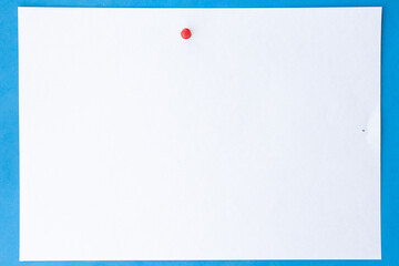 Close up white sheet of paper with red pushpin on blue background for notes