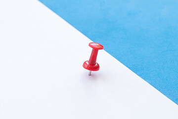 Close up white sheet of paper with red pushpin on blue background for notes