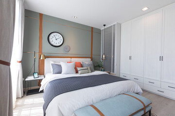 Stylish interior of modern bedroom. White, grey and pastel orange design pillow setting in cozy bedroom with clock on the wall.