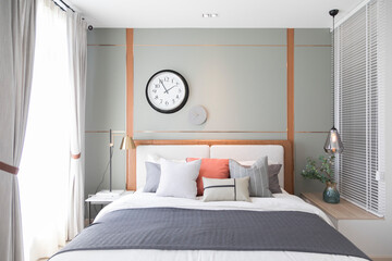Fototapeta na wymiar Stylish interior of modern bedroom. White, grey and pastel orange design pillow setting in cozy bedroom with clock on the wall.