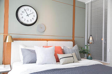 Naklejka premium Stylish interior of modern bedroom. White, grey and pastel orange design pillow setting in cozy bedroom with clock on the wall.