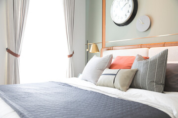 Stylish interior of modern bedroom. White, grey and pastel orange design pillow setting in cozy bedroom with clock on the wall.
