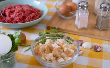 Close up on preparation of  meatballs with raw materials to mix, home kitchen and yellow tablecloth