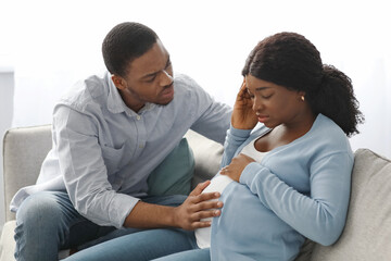Black pregnant lady feeling sick, worried husband sitting by her