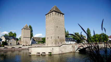 Fototapeta na wymiar Wehrtürme auf der mittelalterlichen Brücke über die Ill mit bedeckter Brücke, ponts couvert, im Viertel von Straßburg petite France, blauer Himmel mit Wolken