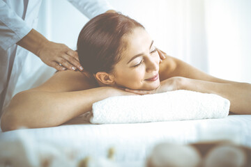 Beautiful brunette woman enjoying back massage with closed eyes. Spa and medicine concept