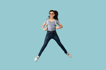 Fototapeta na wymiar Excited Indian teen schoolgirl with backpack jumping up in air on blue studio background