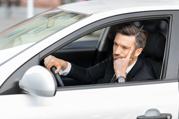 Hopeless middle-aged businessman driving car, stuck in traffic