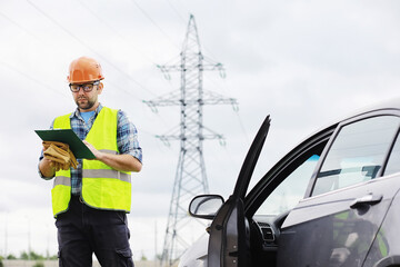 A man in a helmet and uniform, an electrician in the field. Professional electrician engineer inspects power lines during work.