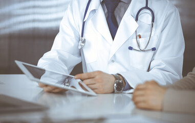 Unknown male doctor and patient woman discussing something while sitting in clinic and using tablet computer. Best medical service in hospital, medicine, pandemic stop