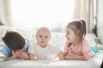 Children lie on the bed next to the newborn baby, little sister.