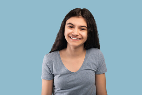 Beautiful Indian teenage girl with dark long hair smiling and looking at camera on blue studio background - Powered by Adobe