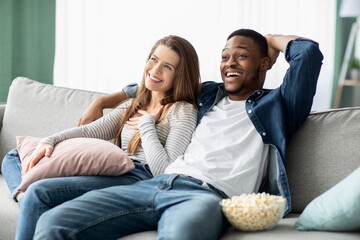 Happy Multiracial Couple Watching Tv And Relaxing On Couch At Home