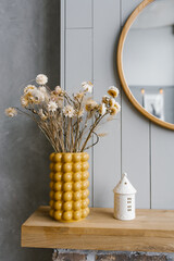 Dried flowers in a yellow ceramic vase in the interior decor of a Scandinavian house with gray...