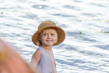 Portrait of little happy caucasian blond boy wearing straw hat against river water in the background. Summer kids fun theme.