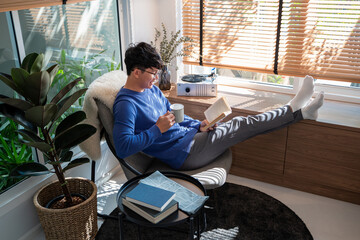 Handsome Asian Man wearing eyeglasses and smiling while Reading Book At Home living room lounge, literature and leisure concept - Powered by Adobe