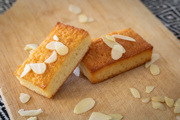 Gros plan sur des gâteaux financiers bien dorés sur une planche à découper parsemé d’amandes...