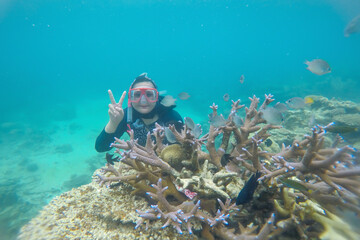 Happy woman snorkeling underwater and posing with a coral reef and fish