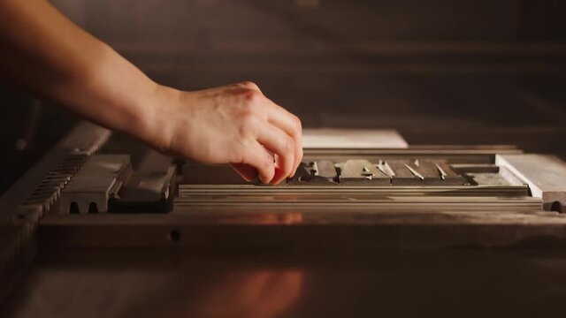 Man putting metal letters together, old printing workshop. Letterpress studio, original, historical hobby. Hands of a an artist, carefully preparing a book for printing, vintage scene.