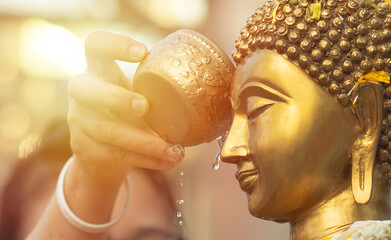 Close up Face of Buddha statue with Hand of sprinkle water onto a Buddha image. Buddhism ceremony,...