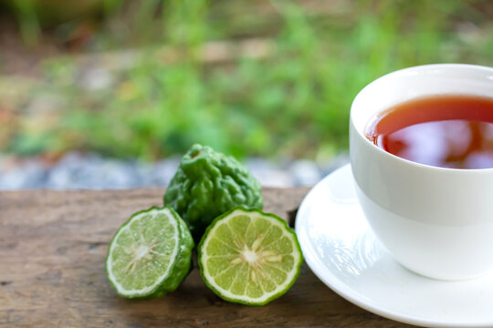 Bergamot tea or Earl Grey tea in white cup and fresh bergamot fruit with sliced on wooden table and blur background.