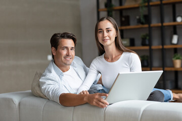 Portrait lovely young couple using a laptop in living room at home.