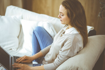 Obraz premium Business woman working on laptop computer sitting indoors during Covid-19 quarantine in cozy living room. Stay at home concept during Coronavirus pandemic