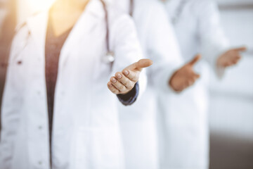 Doctors standing as a team while offering helping hand for shaking hand or saving life in sunny clinic. Medicine concept