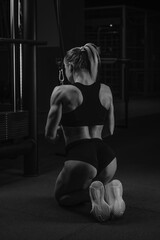 A fit woman with long blonde hair is doing a triceps rope pushdown on her knees in a gym. A girl is training her arms.