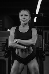 Naklejka premium A fit woman with blonde hair is posing with arms crossed in a gym. A girl is relaxing after a workout.